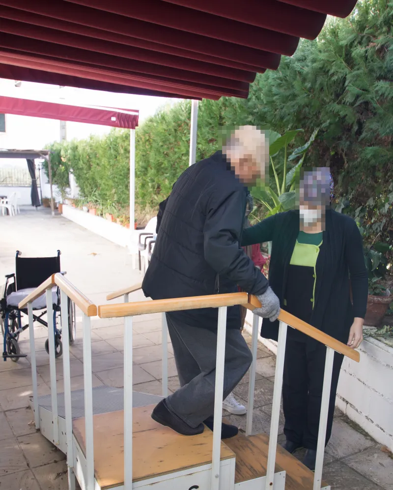 Profesional de Fuenteclara acompañando a un residente en las escaleras de ejercicio del patio